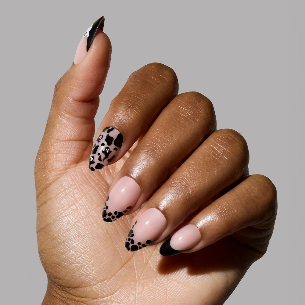A hand with short almond press-on nails, Ghosted by glamnetic, featuring a nude base with black leopard print and black French tips, posed against a plain gray background. - Product image