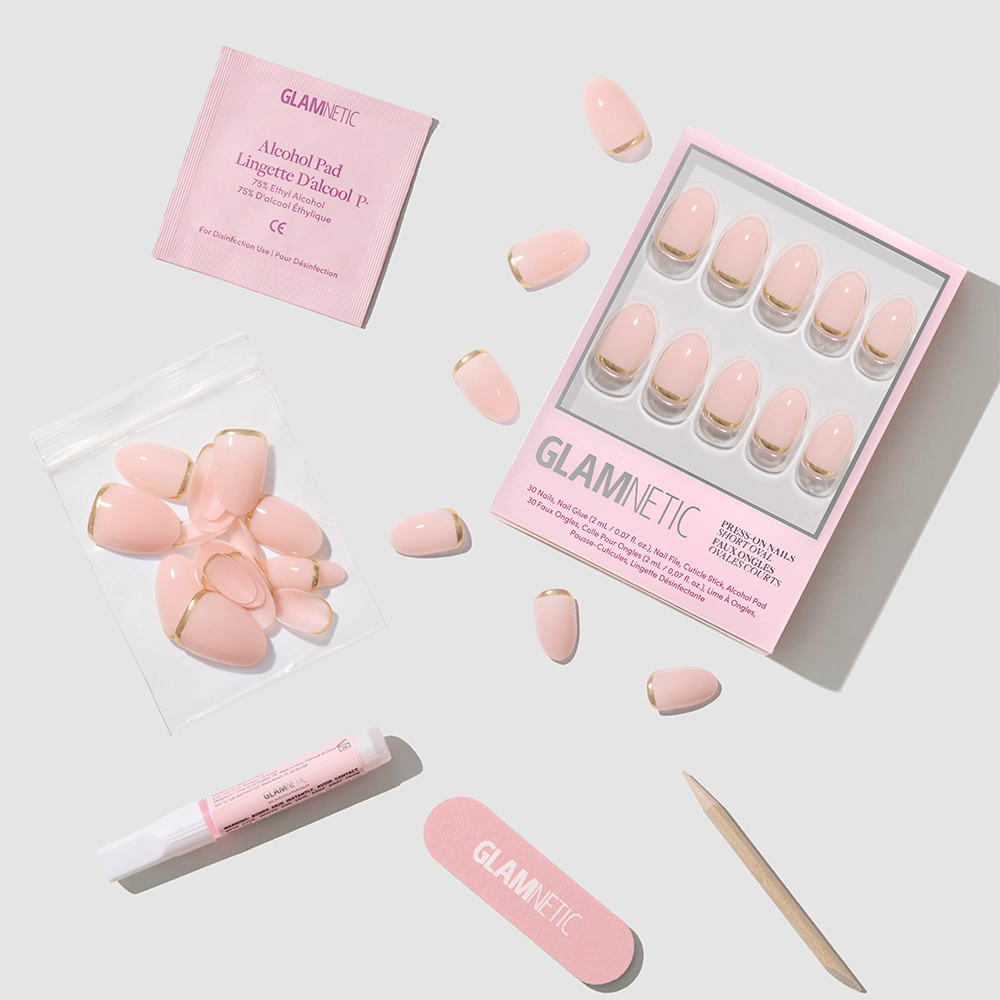 The Glam Goals set by glamnetic features pink short oval press-on nails with gold foil French tips, a pink nail file, glue, alcohol pad, and extra nails, all arranged neatly on a white surface with glamnetic branding. - Product image