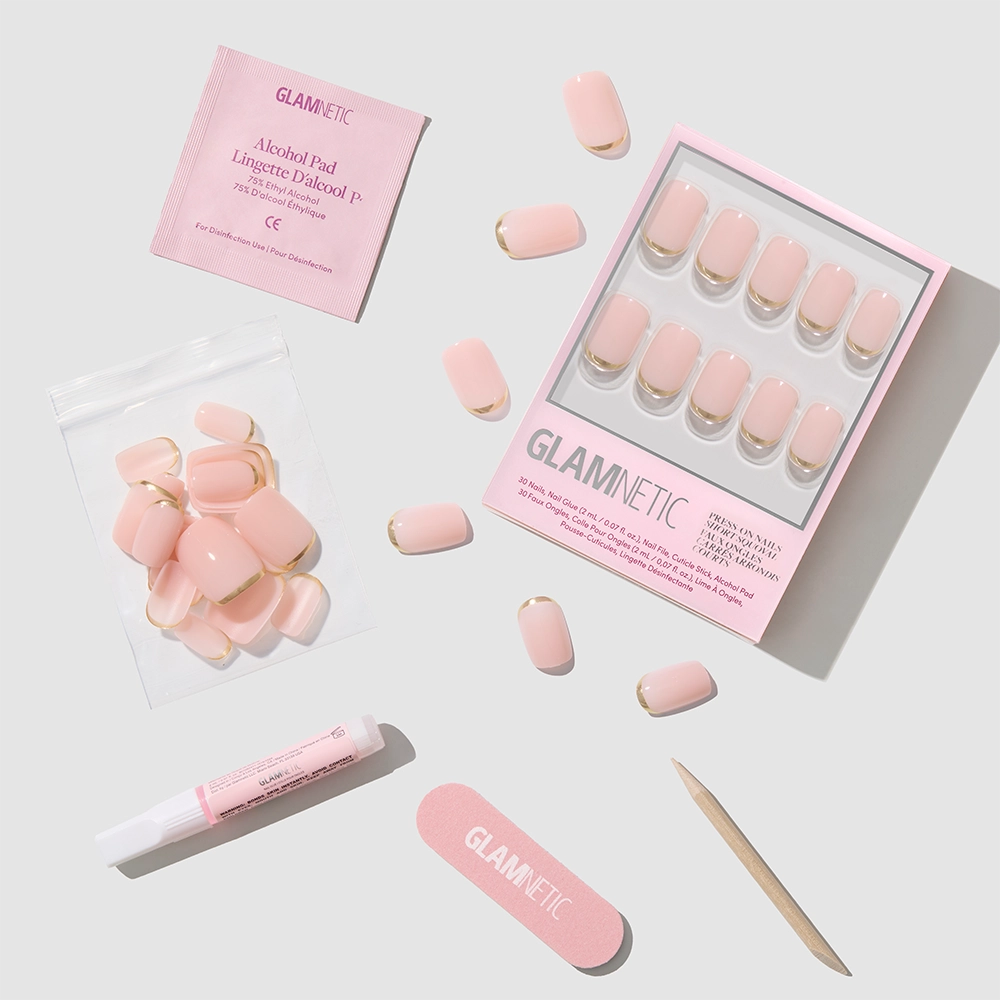 The Goal Setter press-on nails by glamnetic feature short squoval shapes in light pink with gold French tips. Included are an alcohol pad, nail glue tube, wooden cuticle stick, pink nail file, and extra nails—displayed on a light gray background. - Product image