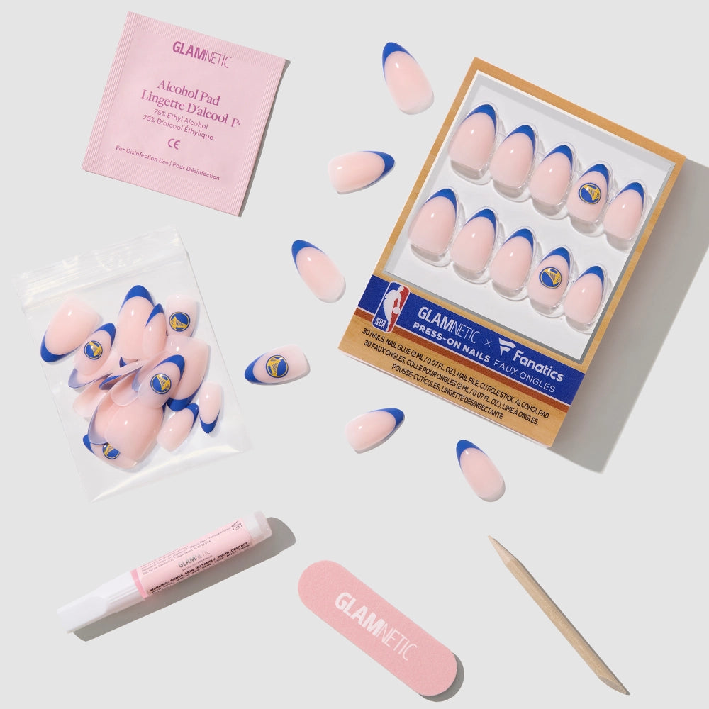 The glamnetic Golden State Warriors Press-On Nail Set features pink and blue nails with the team logo plus a salon-quality kit—alcohol pad, glue, cuticle stick, nail file, and extra French tip almond nails—displayed on a light gray background. - Product image