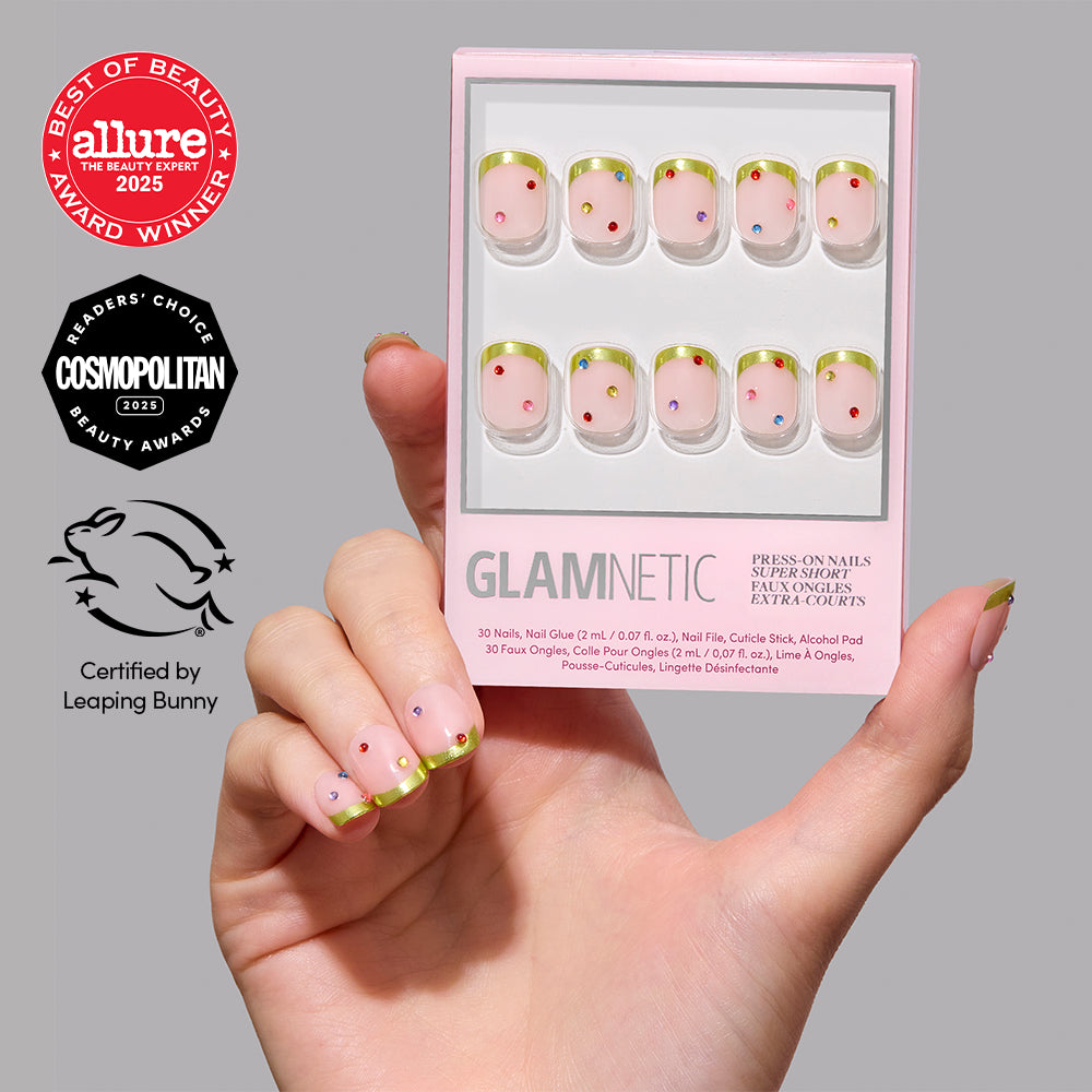 A hand holding a set of Goodie Gumdrops vegan press-on nails featuring a nude base, gold chrome French tips, and small colorful rhinestones. - Product image