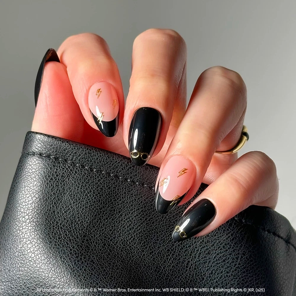 Nude almond-shaped nails with black French tips, featuring gold lightning bolt and round glasses decals from the Harry Potter™ collection by glamnetic. - Product image