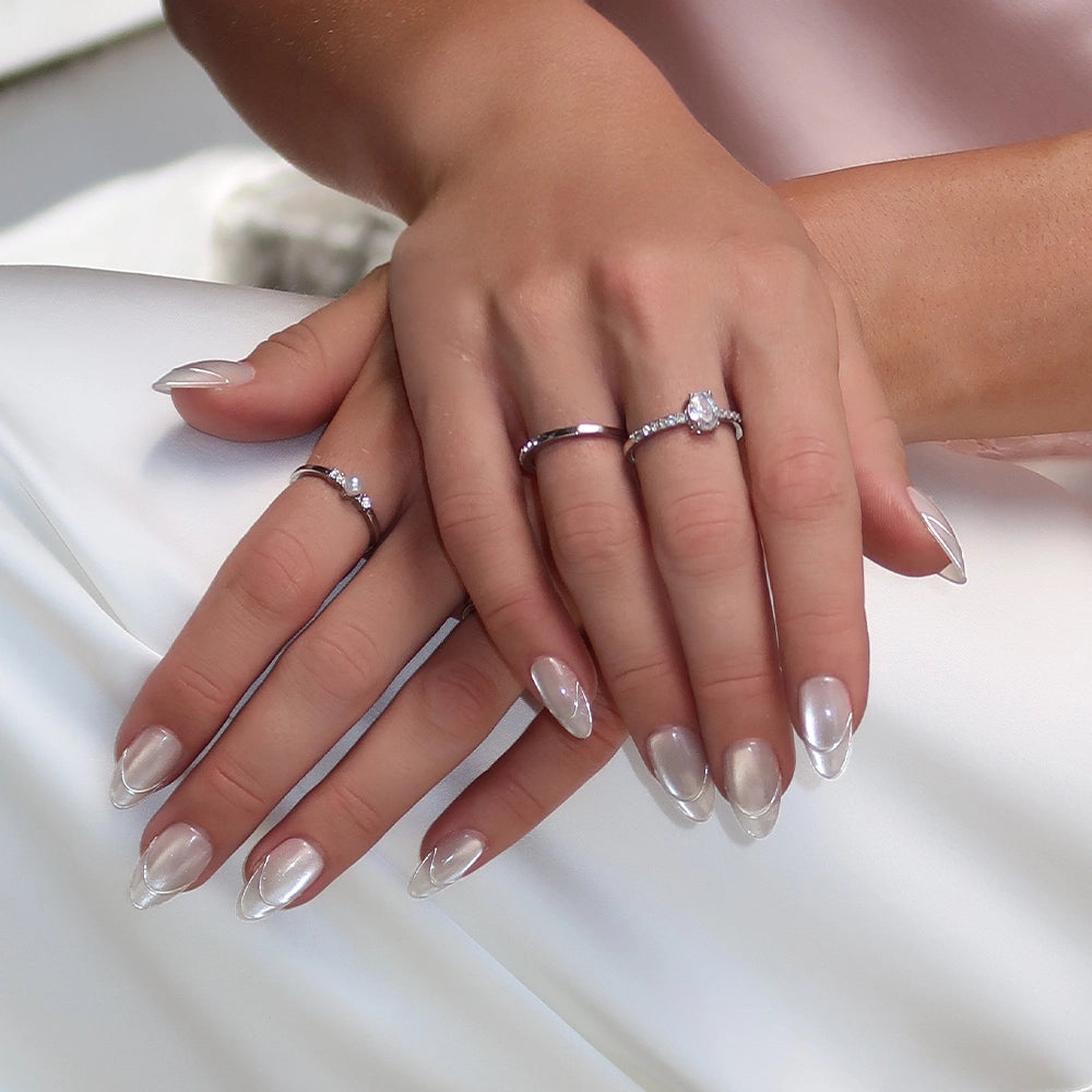 Hands with long, pointed Heavenly Metal press-on nails by glamnetic rest on a white surface. The person is wearing multiple silver rings adorned with small gemstones. - Product image