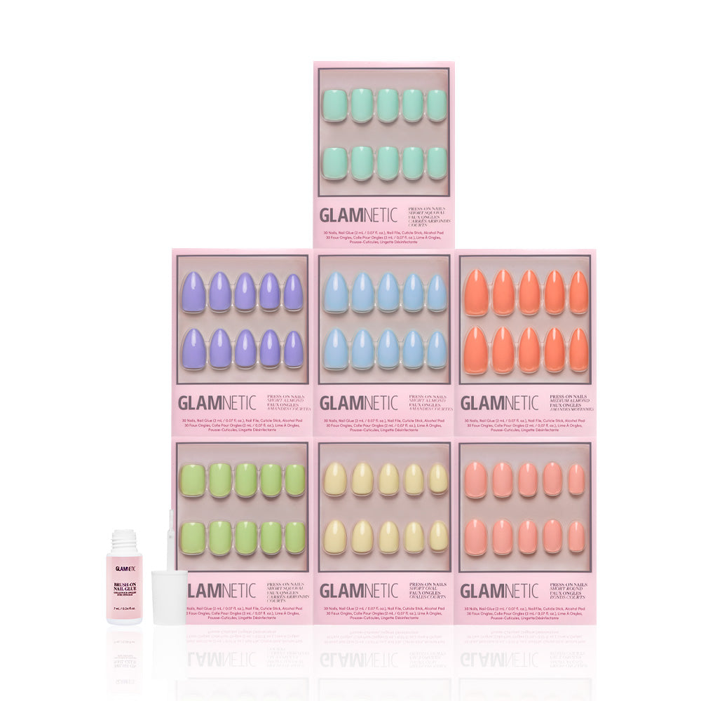 Six pastel Glamnetic press-on nail sets from the Hello Spring Collection are stacked in a pyramid, with a pink nail glue bottle on the left. Each set comes in a glossy pink box and features vibrant pastel solid shades. - Product image