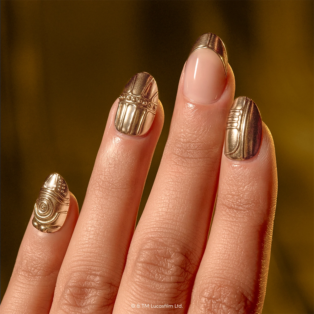 Help! I Think I’m Melting! - A hand with manicured nails features four gold metallic designs inspired by C-3PO from Star Wars using glamnetic’s “Help! I Think I’m Melting!” press-on nails, while one nail is left plain and natural.