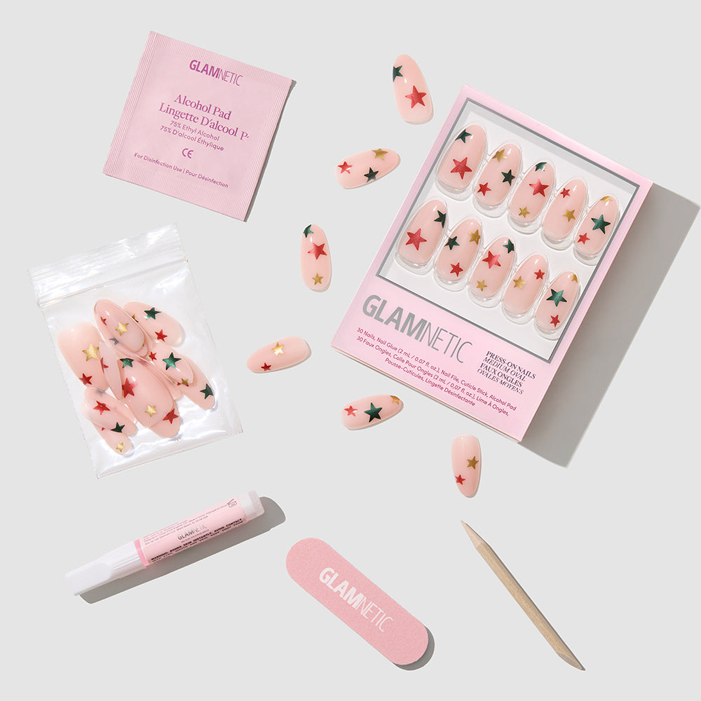 Holiday Wish - Glamnetic Holiday Wish almond-shaped press-on nails featuring red and green stars, with an alcohol pad, glue, nail file, and wooden cuticle stick arranged on a white background for a salon-quality manicure.