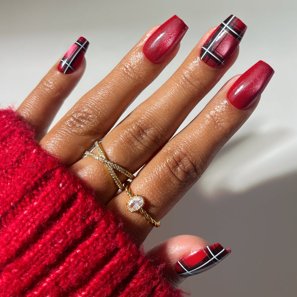 Hand with Holiday Tartan coffin press-on nails featuring a red, black, and white tartan pattern and solid red shimmer polish.