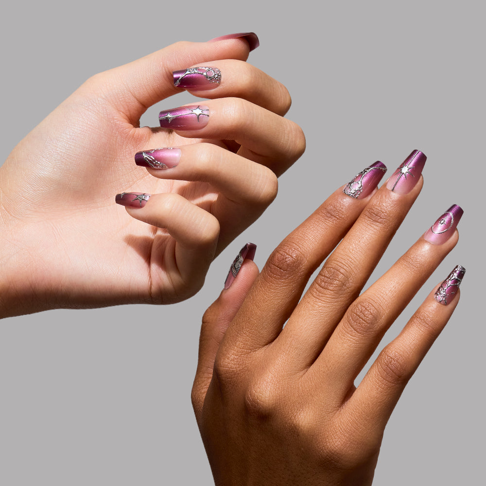 Two hands showcase the Immortal Kiss coffin nail set by glamnetic, with manicured nails featuring glossy ombre shades of purple adorned with silver rhinestones and metallic accents. The elegant, modern look is highlighted against a plain gray background. - Product image