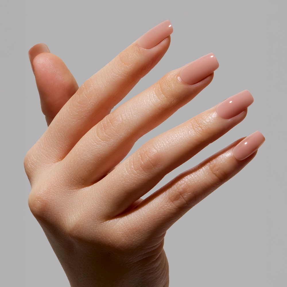 A close-up of a hand with long, square nails in a glossy nude-pink ombré minimalist manicure, featuring In The Nude by glamnetic, against a plain light gray background. - Product image