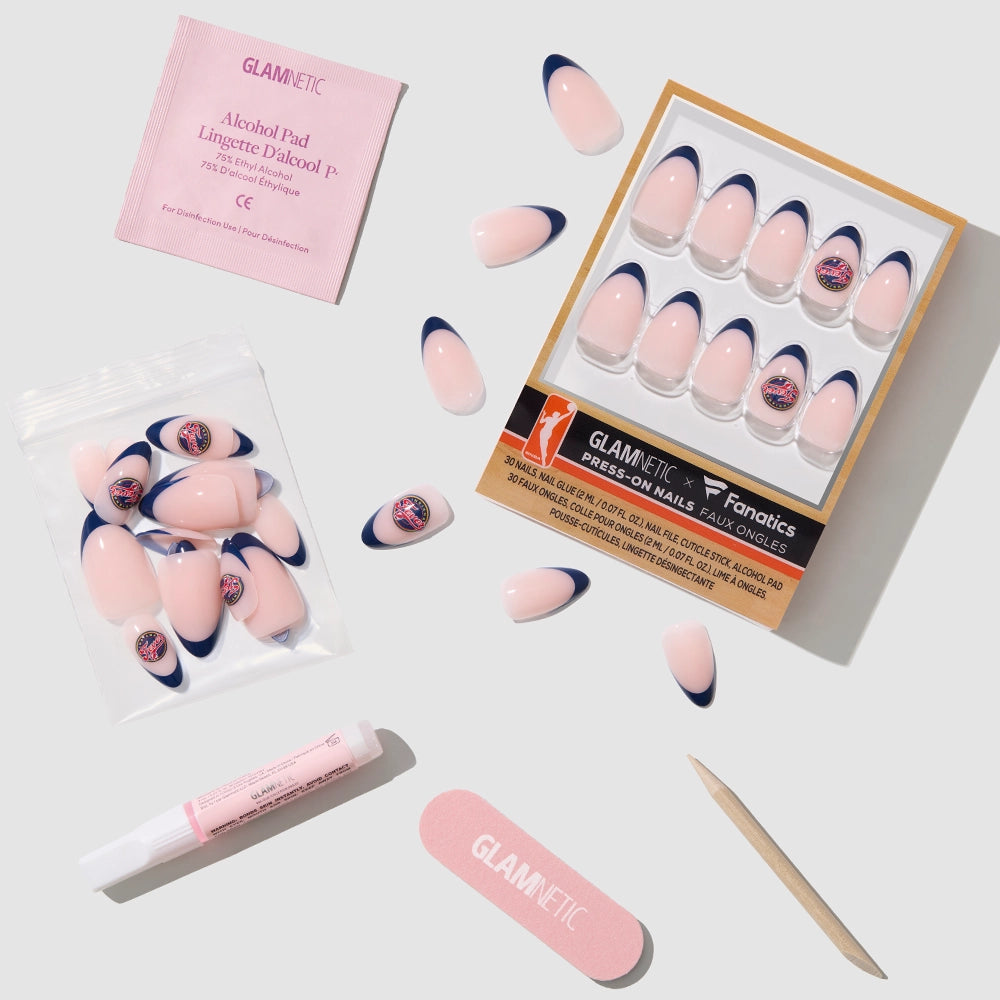 The glamnetic Indiana Fever Press-On Nail Set includes pink nails with navy-blue French tips, extra nails, glue, an alcohol pad, nail file, and cuticle stick—salon quality essentials arranged neatly on a light background. - Product image