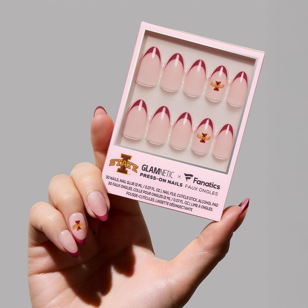 A hand holds a glamnetic Iowa State Cyclones Press-On Nail Set with pink bases, dark red tips, and ISU logos. The box displays ten salon-quality nails arranged neatly for dedicated Cyclone fans.