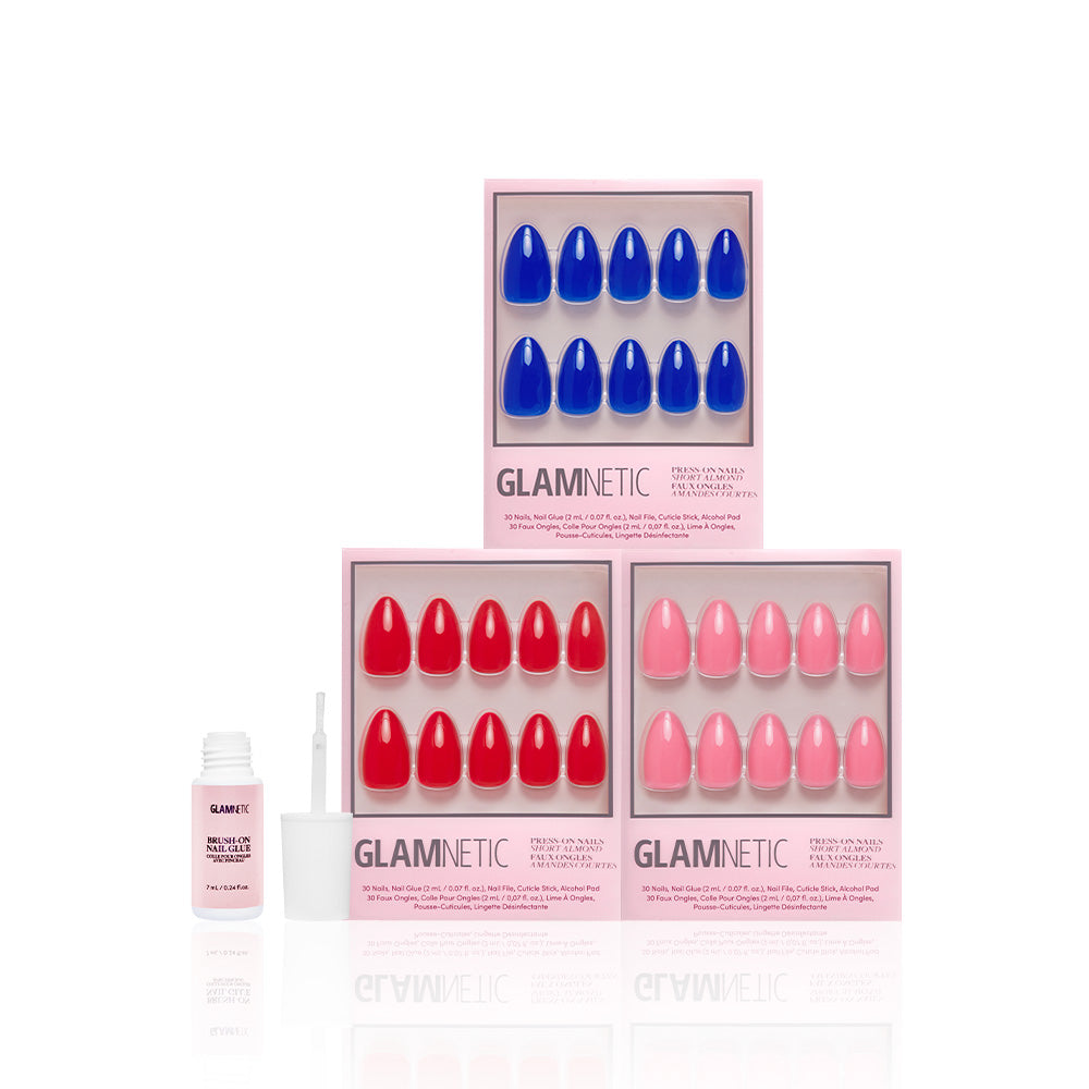 Three boxes of glamnetic It Girl Summer press-on nails are displayed upright in Cobalt Blue, Fiery Red, and Flamingo Pink. In front is an open nail glue bottle with a brush applicator, all shown against a white background. - Product image
