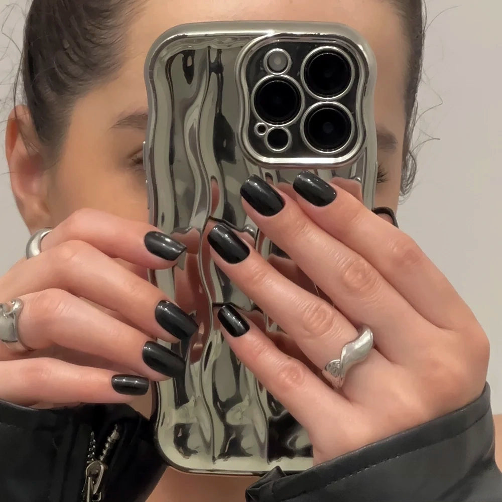 Jet Black - Wearing Jet Black by glamnetic and silver rings, a person holds a wavy, reflective silver phone case that partially covers their face.
