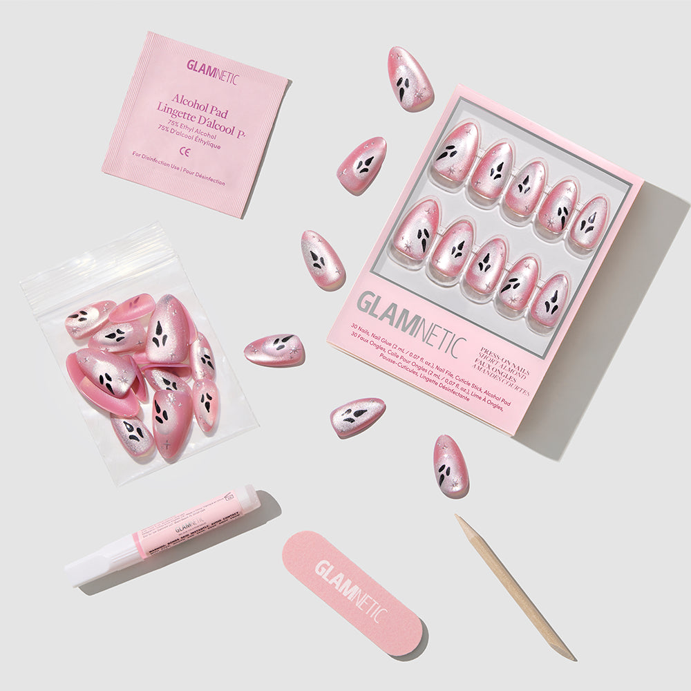 Just A Ghoul press-on nails from glamnetic, featuring a pink and white watermelon seed design with a luxurious velvet finish, are arranged on a light gray surface. The box includes everything you need for the perfect short almond manicure at home: glue, a nail file, wooden stick, alcohol pad, extra nails, and is labeled glamnetic. - Product image