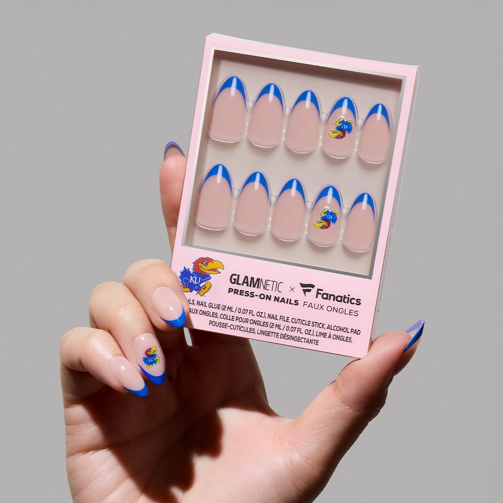 A hand holds the glamnetic Kansas Jayhawks Press-On Nail Set, featuring a nude base, blue French tips, and the University of Kansas Jayhawks logo. One nail on the hand also displays this design.