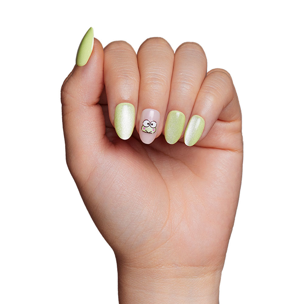 A hand with light green, almond-shaped reusable nails; the ring fingernail shows a cartoon face with big eyes and a silly expression on nude, inspired by glamnetic’s Keroppi™ Nail Set. - Product image
