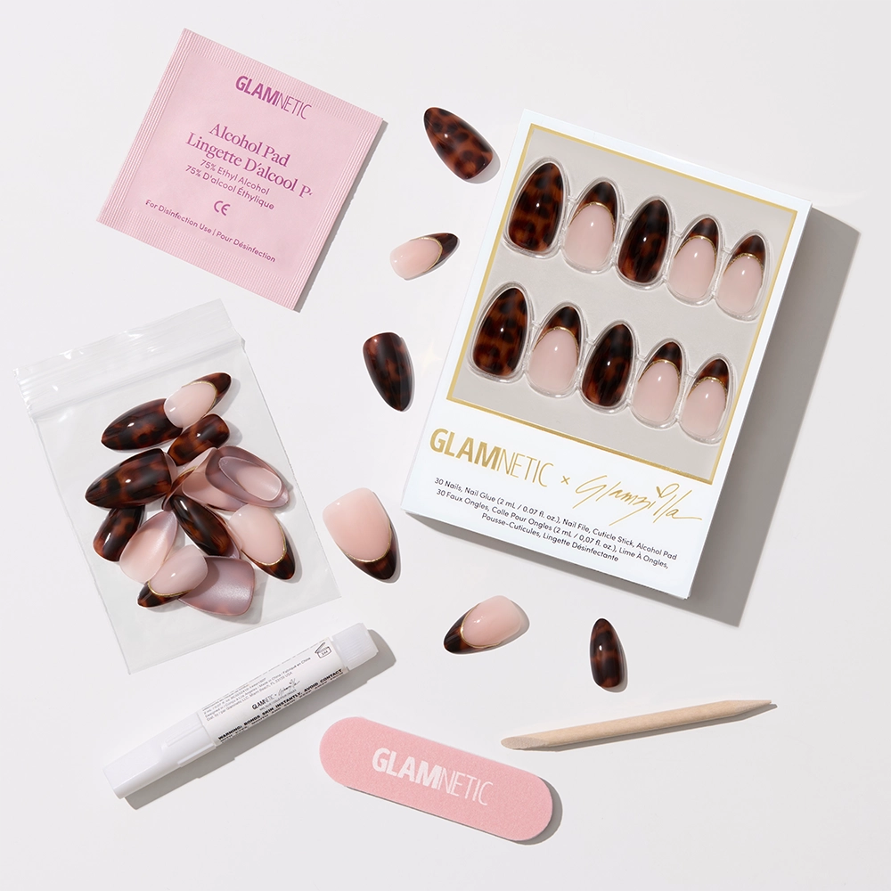 Flat-lay of the full Glamnetic x Glamzilla press-on nail kit, including the boxed set of 30 nails, individual loose nails, nail glue, a wooden cuticle stick, an alcohol pad, and a pink nail file with the Glamnetic logo.

 - Product image