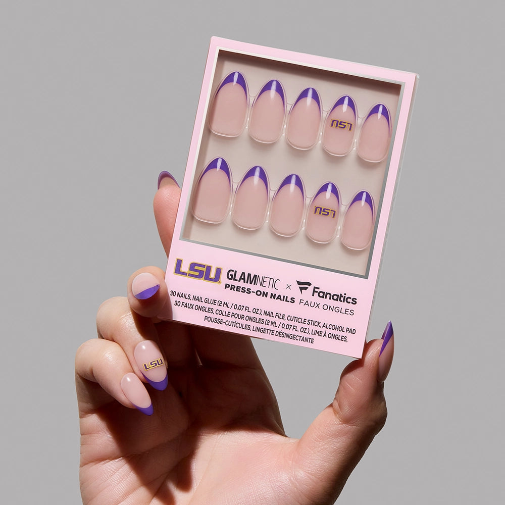 A hand holds a box of glamnetic LSU Tigers Press-On Nail Set featuring nude nails with purple and gold French tips and the LSU logo; the person’s nails match the press-ons in the box.