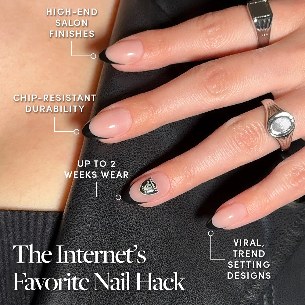A hand with almond-shaped nails in the Las Vegas Raiders Press-On Nail Set by glamnetic, featuring a French fan manicure, graphic accent nail, high-end finish, chip resistance for up to 2 weeks. Silver rings add style for Raiders fans. - Product image