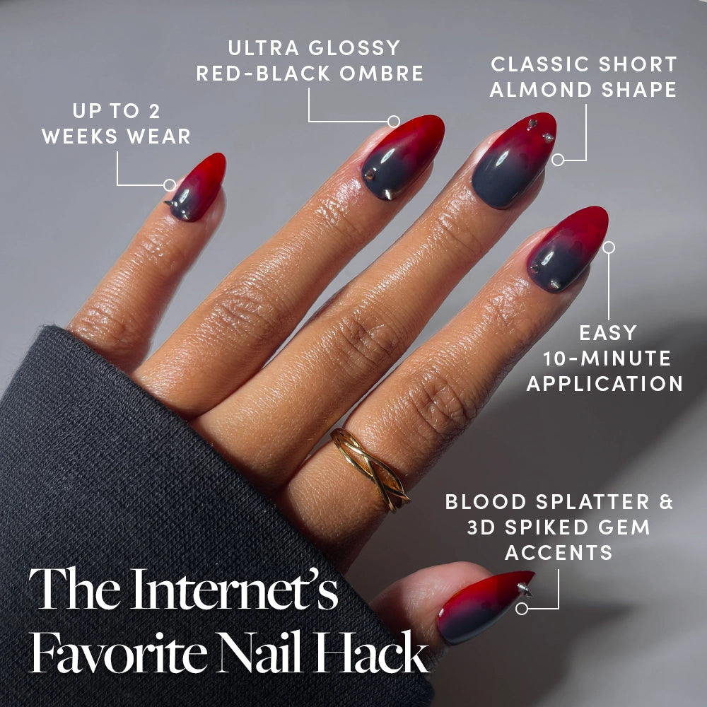 A hand with short almond-shaped nails in a red-black ombre design, glossy finish, spiked gems, and blood splatter accents showcases the Lil Devils Press-On Nails by glamnetic. Labeled with text highlighting features like 2-week wear and 10-minute application, these striking red jewelry nails are perfect for making a bold statement on any occasion. - Product image