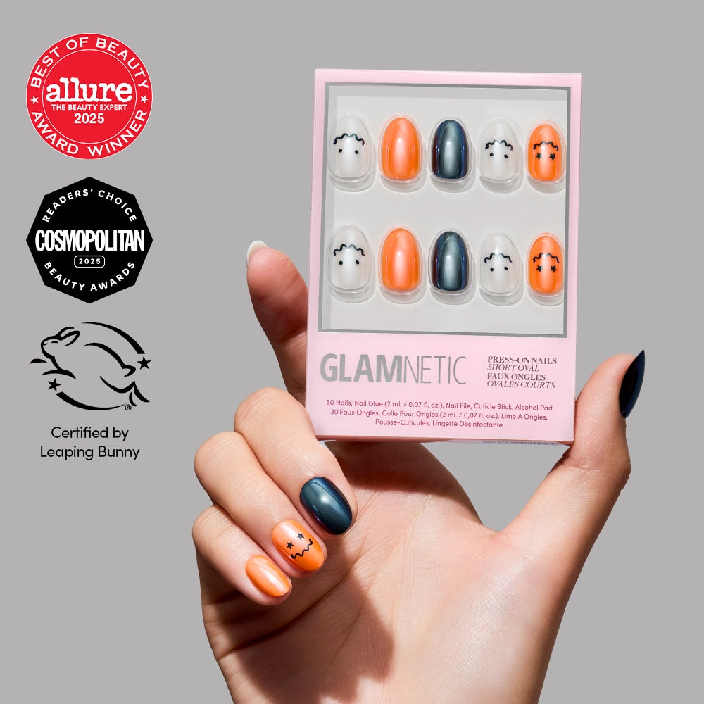 A hand with Halloween-themed press-on nails holds the Glamnetic Lil Gremlins nail kit. The kit features short oval nails in orange and black with cute bat designs and a stunning glazed finish. Beauty award and cruelty-free certification logos appear on the left. - Product image