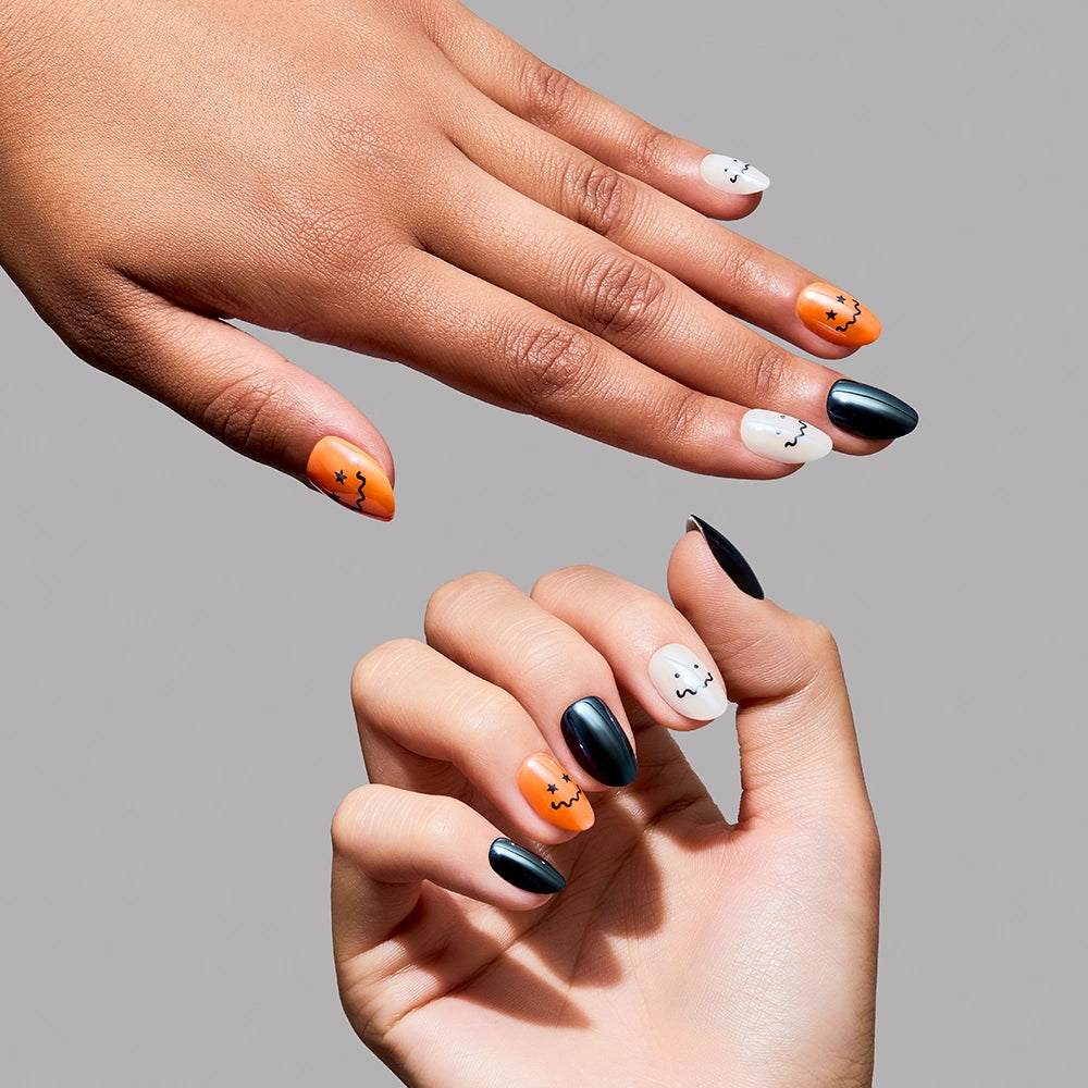 Two hands with almond-shaped nails against a grey background showcase the “Lil Gremlins” press-ons by glamnetic. The manicure features a mix of glossy black, orange, and off-white polish with a striking glazed finish, while select nails are adorned with minimalist black face or star designs for a playful Halloween vibe. - Product image