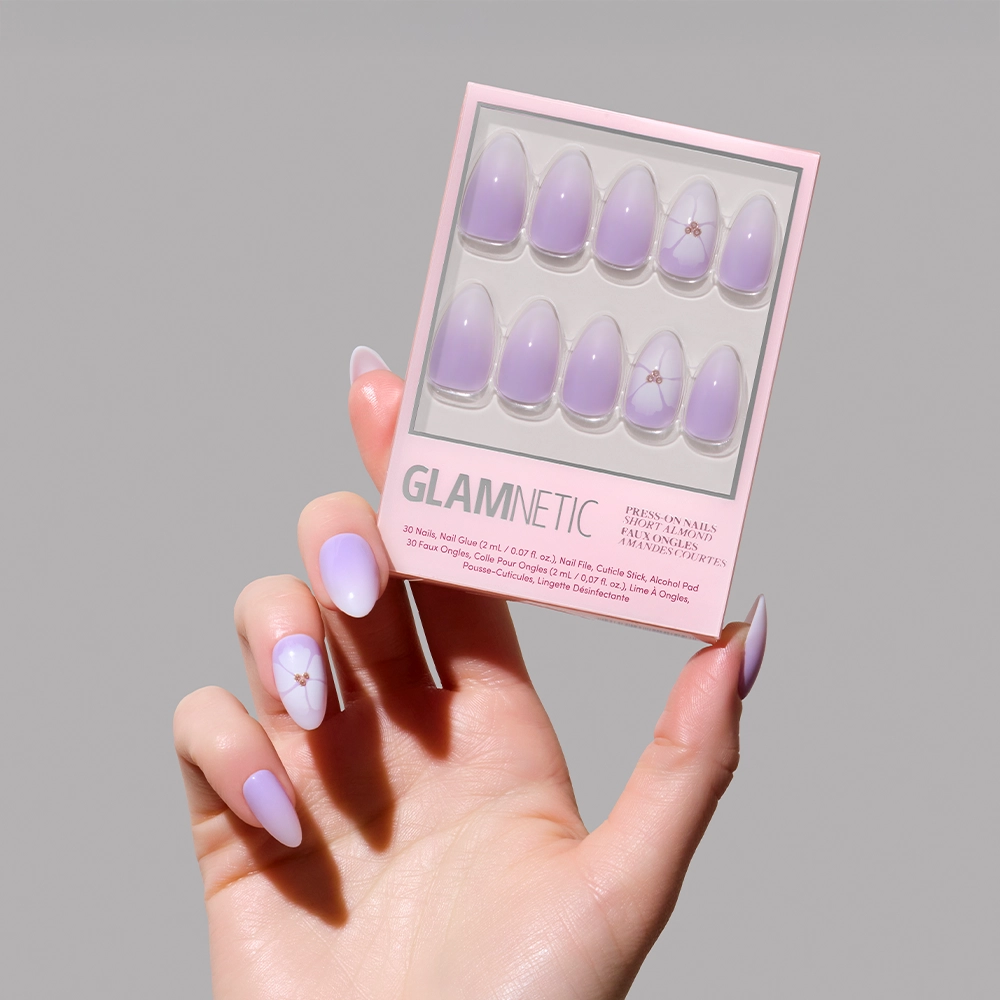 A hand with pastel purple almond nails holds a matching box of glamnetic’s Lilac Reef, featuring a dreamy lavender ombré design and a small star accent on one nail.