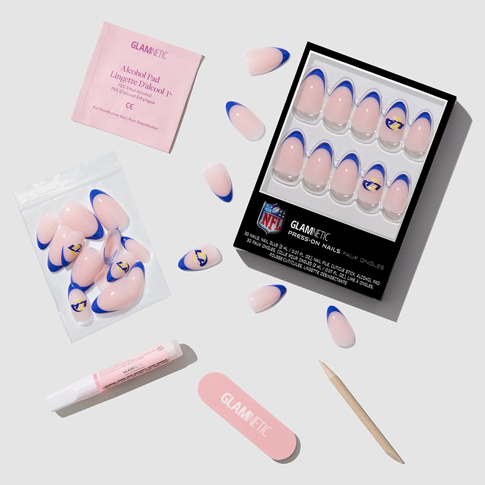 Show your team pride with the glamnetic Los Angeles Rams Press-On Nail Set, featuring blue French tips, Rams logos, a pink nail file, cuticle stick, nail glue, alcohol pad, extra nails—all on a light gray background. - Product image