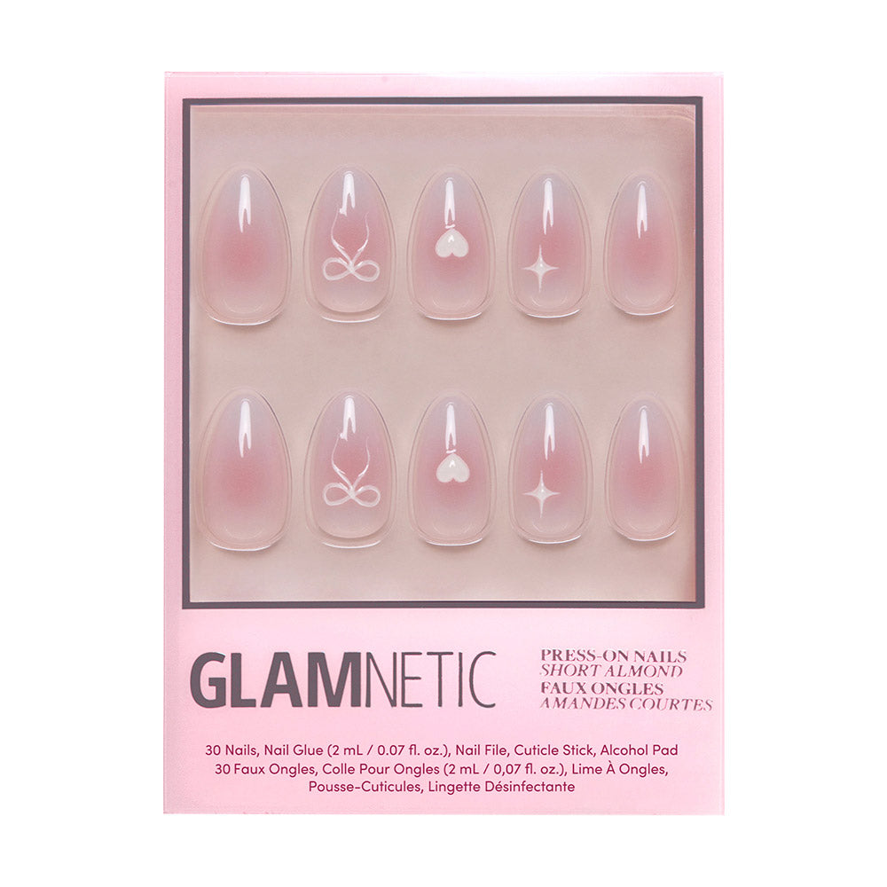 A box of glamnetic Lovers Knot short almond nails in a semi-transparent pink gradient, featuring white hearts and 3D bows on select nails. The set includes 30 nails plus nail care accessories.