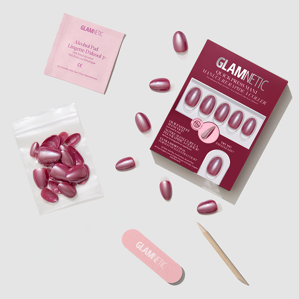 The Mauve Muse press-on nails set by glamnetic includes mauve nails, nail glue, a wooden cuticle stick, a pink nail file, an alcohol pad, and extra nails, all arranged neatly on a light gray surface. - Product image