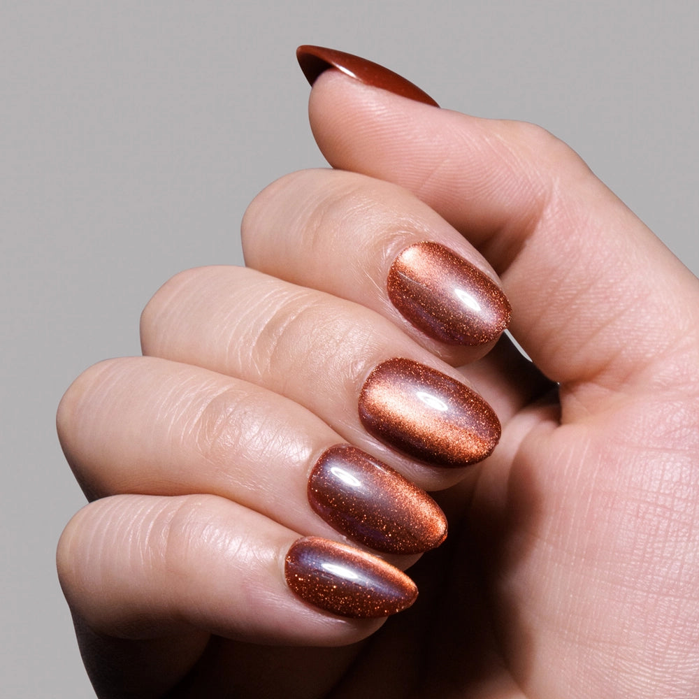 A hand with almond-shaped cat-eye nails painted in glamnetic’s Magnetic Moscow, a shimmery metallic copper shade, shown against a plain gray background. - Product image