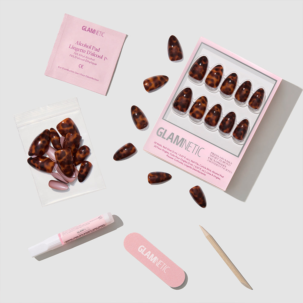 The glamnetic Main Reference set includes almond-shaped press-on nails with a brown tortoiseshell design, a pink nail file, wooden cuticle stick, nail glue, alcohol pad, and extra nails—all displayed on a white background. - Product image
