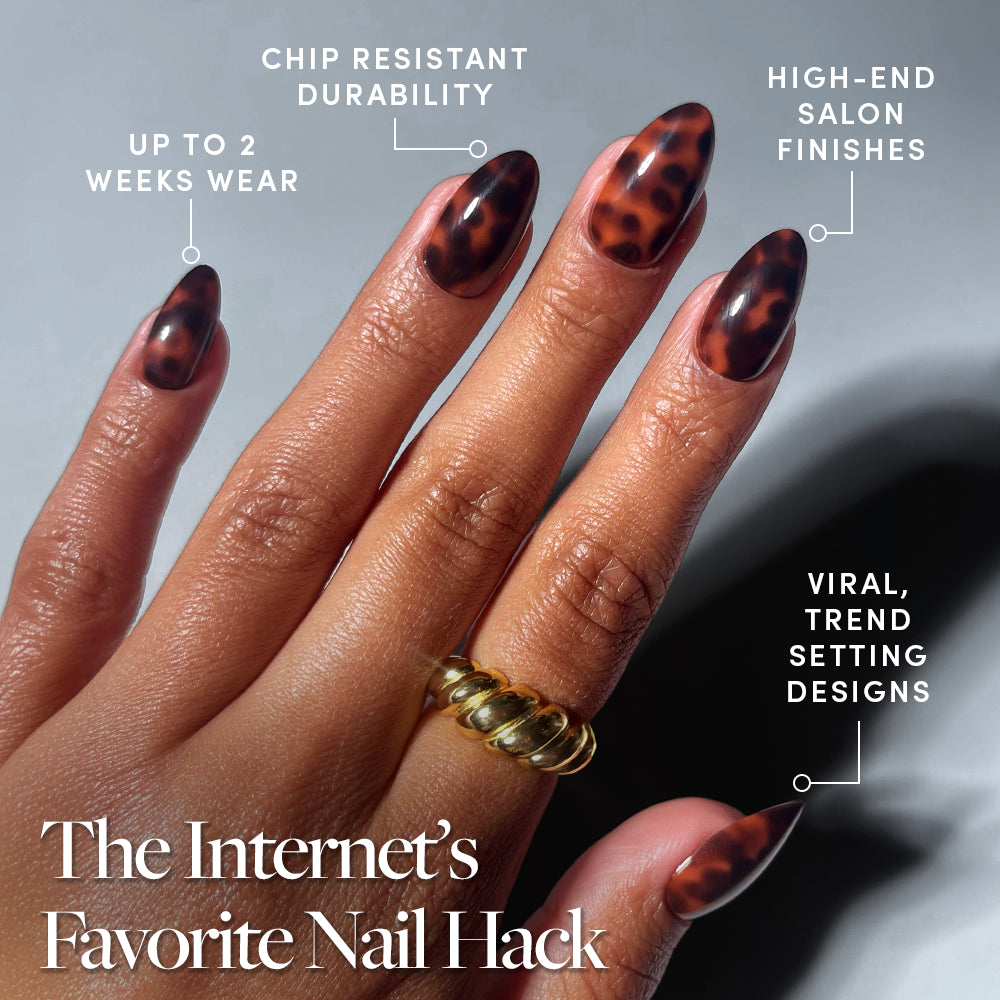 A hand with gold rings displays glamnetic’s Main Reference press-on nails in a long almond shape and tortoiseshell design—offering up to 2 weeks wear, chip-resistant durability, salon-quality finish, and trend-setting style. - Product image