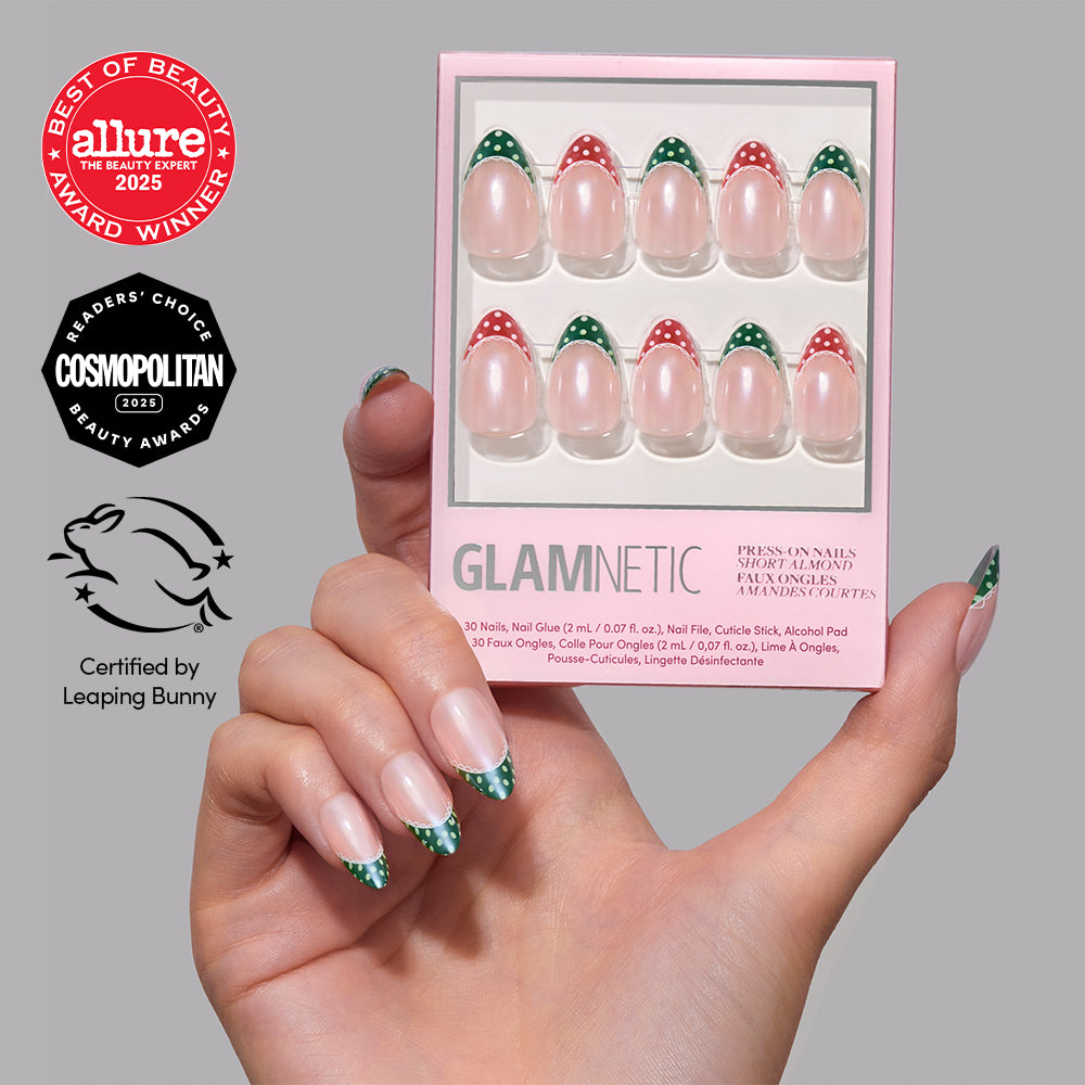 A hand holds a box of Glamnetic Matching PJs short almond-shaped press-on nails featuring red and green polka-dot French tips, displayed next to Allure and Cosmopolitan award logos for a festive holiday mani. - Product image