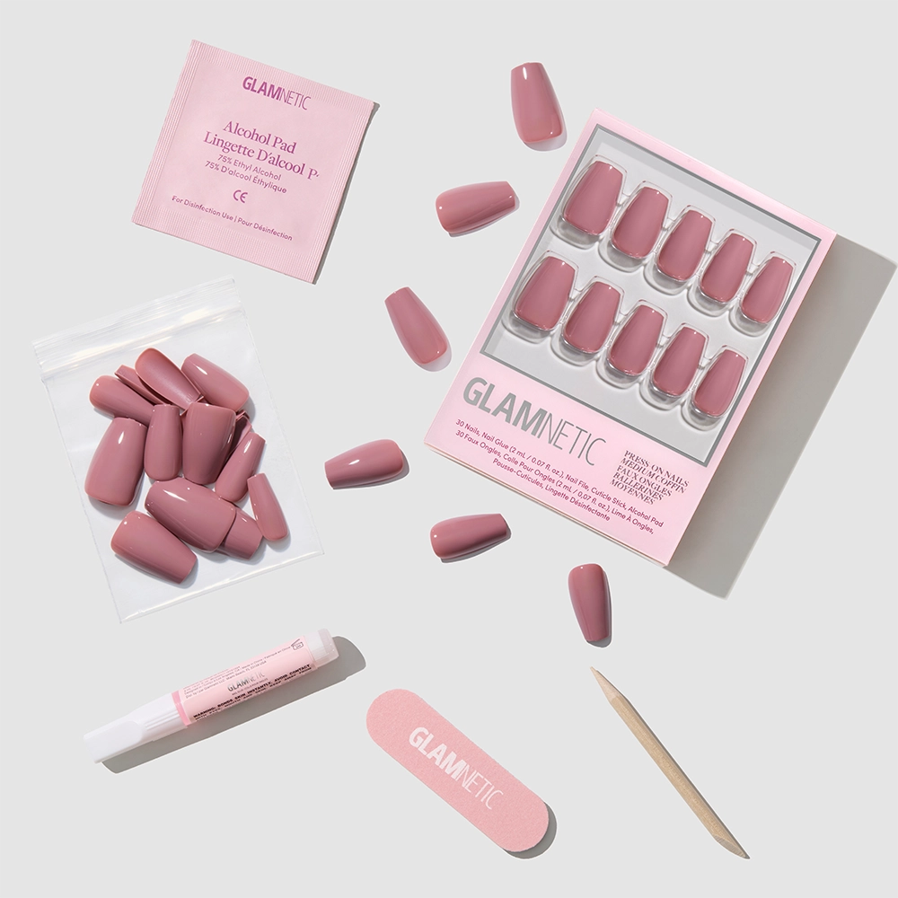 Mauve Affair by glamnetic: glossy pink medium coffin fake nails, nail file, wooden cuticle stick, glue tube, alcohol pad, and extra nails—all arranged on a light gray surface with glamnetic packaging. - Product image