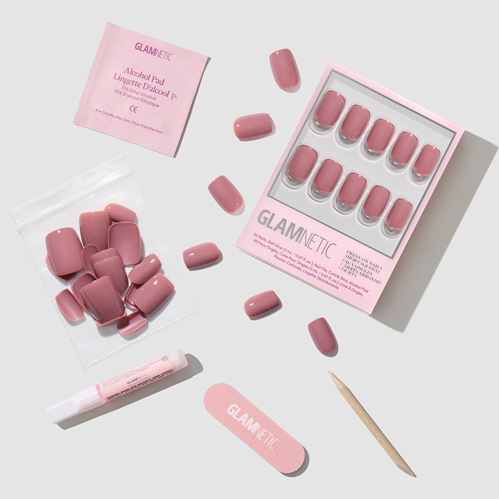 The glamnetic Mauve On set features pink short squoval press-on nails with accessories—alcohol pad, nail glue, nail file, cuticle stick, and extra nails—all arranged neatly on a light gray surface. - Product image