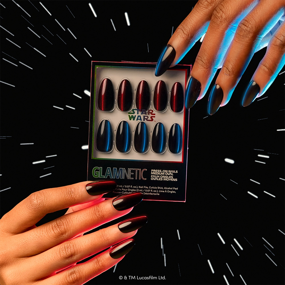 Hands with long black nails hold glamnetic’s “May The Force Be With You” press-on nail set, showcasing black, red, and blue designs inspired by iconic lightsabers and finished with a sleek velvet top coat, against a star-filled, space-like background. - Product image