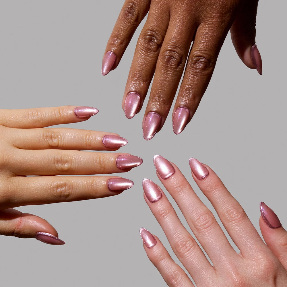 Three pairs of hands with different skin tones show off glamnetic Mertini Pink Press-On Nail Sets—almond-shaped, shiny, with subtle metallic foil accents—against a plain grey background. - Product image