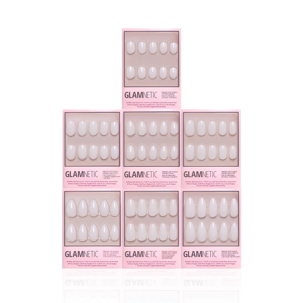 Seven boxes of glamnetic's Milky Manis Bundle in light pink packaging are arranged in a pyramid on a white background. Each box reveals semi-transparent, glossy white press-on nails inside. - Product image