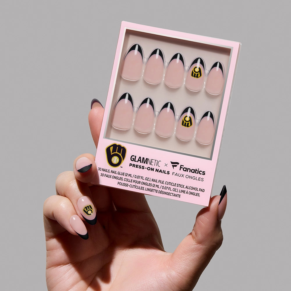 A hand holds a glamnetic Milwaukee Brewers Press-On Nail Set box with pink and black French tip nails featuring the team logo on both the packaging and nails, highlighted by collaboration branding.
