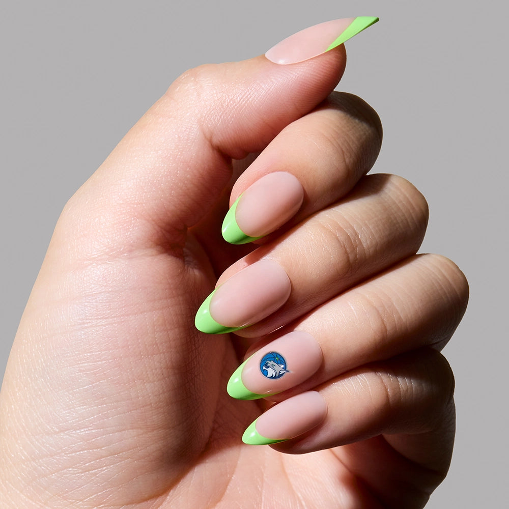 A hand wears the glamnetic Minnesota Lynx Press-On Nail Set, featuring long almond-shaped nails with a light nude base, neon green French tips, and a blue and white swirl design on the ring finger against a plain gray background.