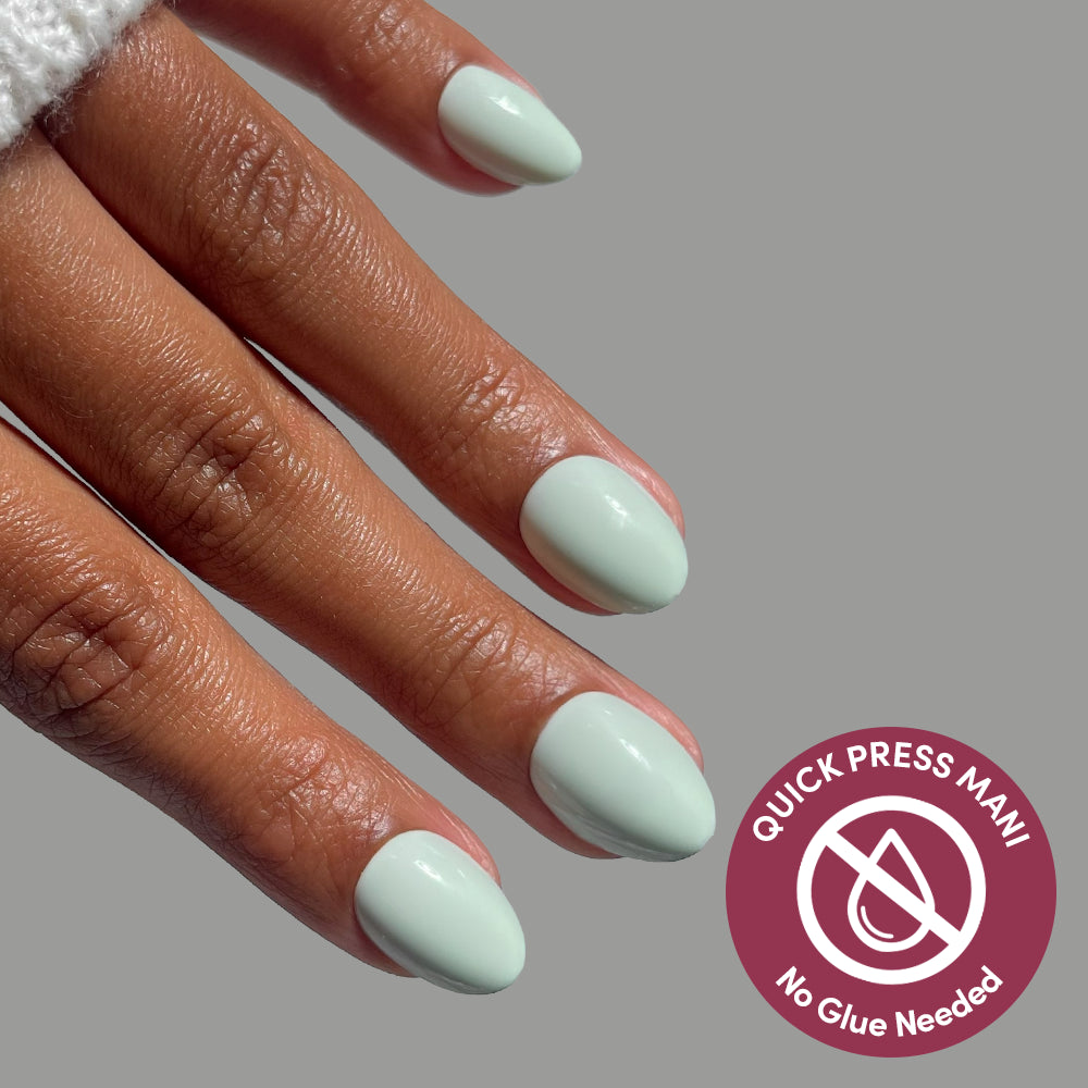 A hand with extra short oval mint green Minty Cloud press-on nails next to a circular Glamnetic badge that reads Quick Press Mani, No Glue Needed with a crossed-out glue drop icon. - Product image