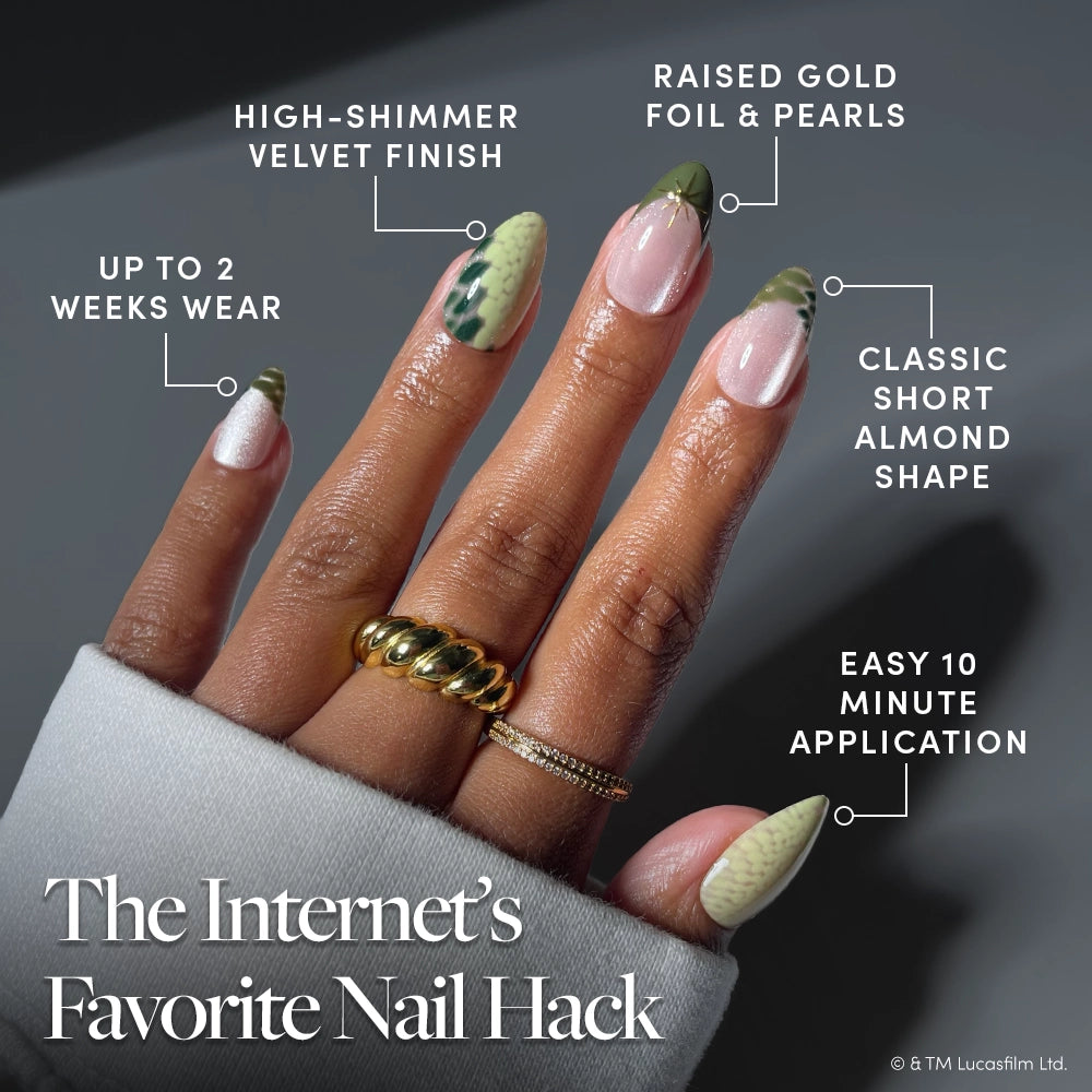 Much To Learn, You Still Have - A hand with almond-shaped, high-shimmer nails from glamnetic’s “Much To Learn, You Still Have,” featuring pearl and gold accents. Labels highlight features like two-week wear, easy application, and a velvet finish. The hand is adorned with chunky gold rings—a celestial look perfect for short almond nail fans or anyone wanting to try Star Wars-inspired press-ons. Text reads: The Internet’s Favorite Nail Hack.