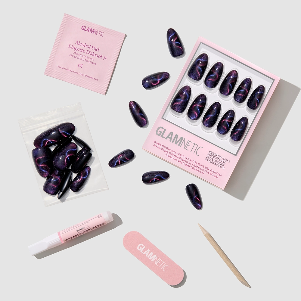 A flat lay of glamnetic Mystic Topaz press-on nails in a dark purple and pink design, with an alcohol pad, nail glue, nail file, cuticle stick, and extra iridescent nails neatly displayed on a light background. - Product image