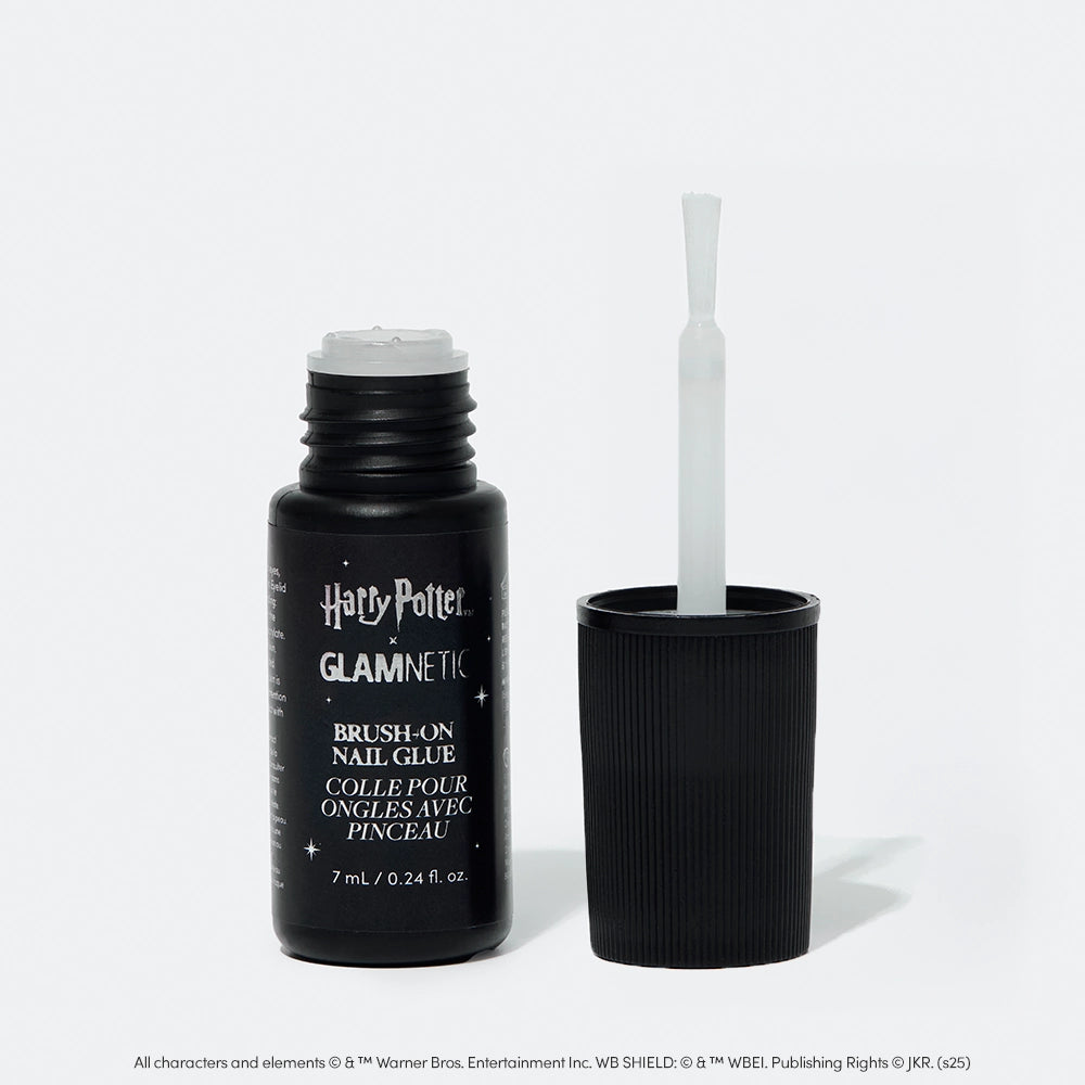 A black bottle of glamnetic Harry Potter™ x Glamnetic Brush-On Nail Glue stands upright with the cap off, showing its brush applicator—ideal for press-on nails. The label displays both English and French text.