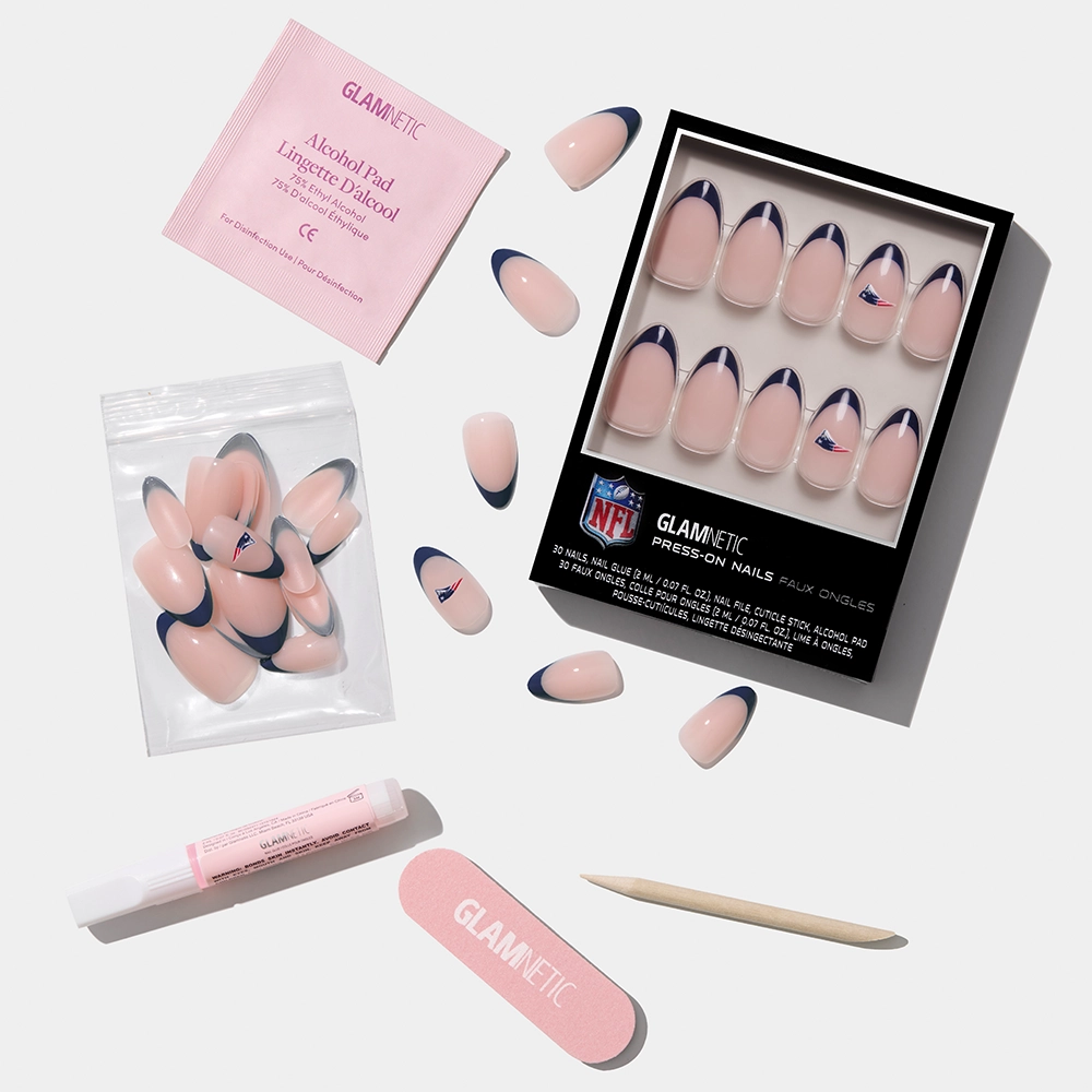 The glamnetic New England Patriots Press-On Nail Set includes nails with a pink base and dark blue tips, extra nails in a plastic bag, a nail file, cuticle stick, glue, and an alcohol pad, all arranged on a white surface. - Product image
