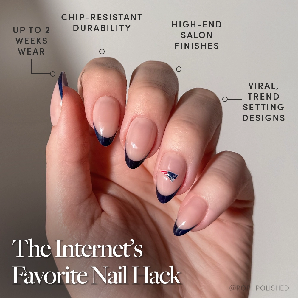 A hand with a nude and navy blue French manicure, featuring the New England Patriots Press-On Nail Set by glamnetic, is shown. Text highlights chip-resistant durability, up to two weeks wear, salon-quality finish, and trendy designs. The Internet’s Favorite Nail Hack. - Product image