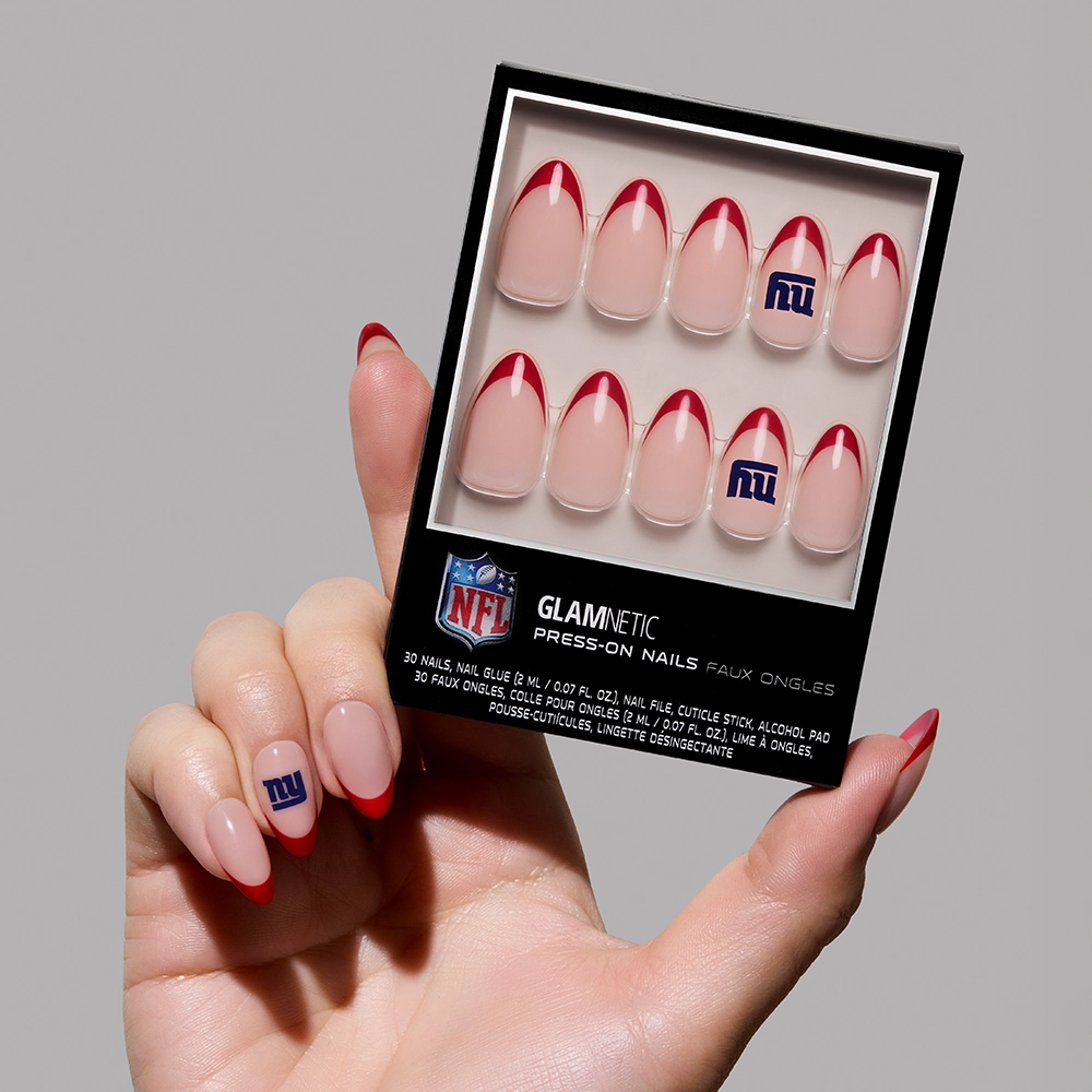 A hand holds a box of the New York Giants Press-On Nail Set by glamnetic, featuring French tips with red accents and Giants logos—perfect for fans wanting stylish team-themed nails.