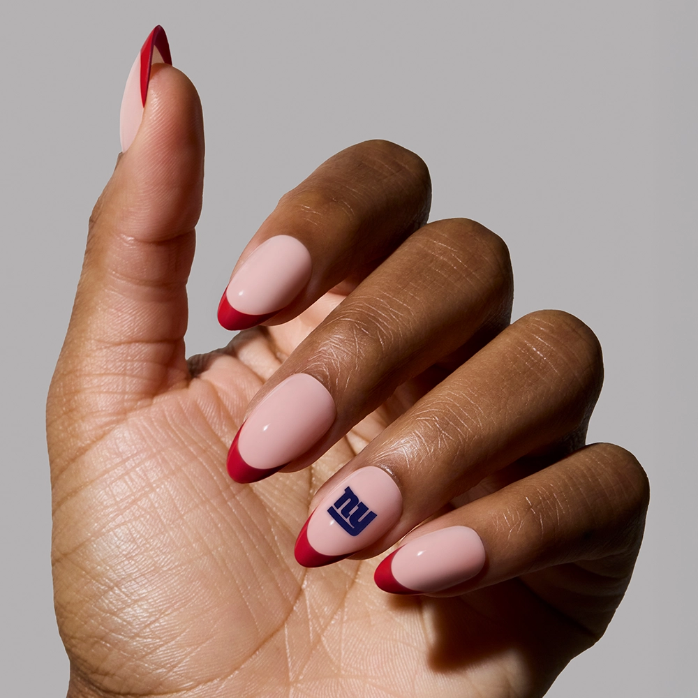 Show off your NFL spirit with glamnetics New York Giants Press-On Nail Set—light pink almond nails with red tips and a blue NY logo on the ring finger. Perfect for fans, all set against a simple gray background. - Product image