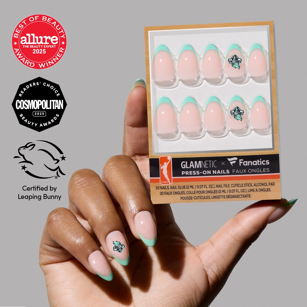 A hand with mint green French tip press-ons holds the New York Liberty Press-On Nail Set by glamnetic. The packaging shows Glamnetic x Fanatics branding plus Allure, Cosmopolitan, and Leaping Bunny certification logos.